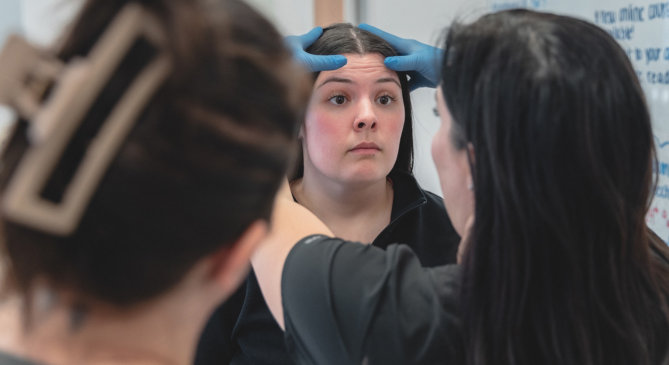 Woman receiving facial treatment with gloved hands.